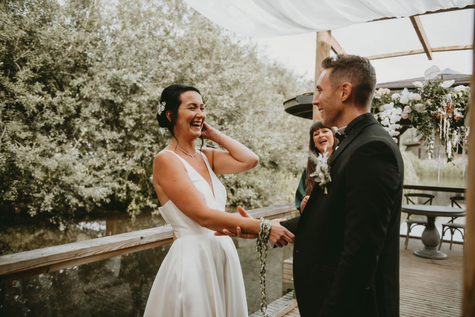 Celebrant-led Handfasting ceremony with laughing bride and groom outdoors by a lake